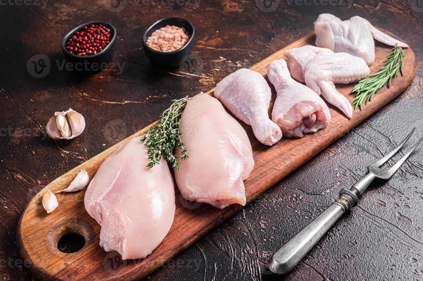 Raw chicken meat, assortment of parts - drumstick, breast fillet, wings, thigh with spices. Dark background. Top view photo