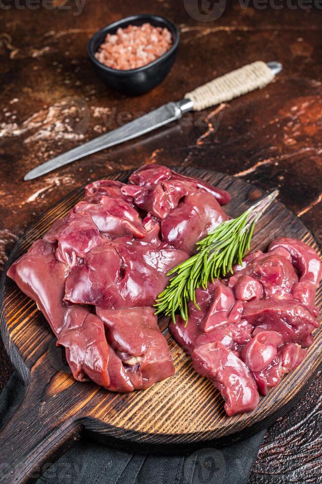Sliced Raw chicken liver, fresh fowl offals on wooden board. Dark background. Top view photo
