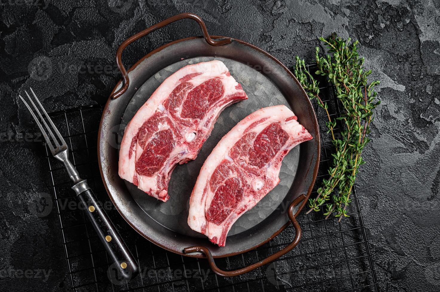 Raw fresh lamb loin chops with herbs and spices in steel tray. Black background. Top view photo