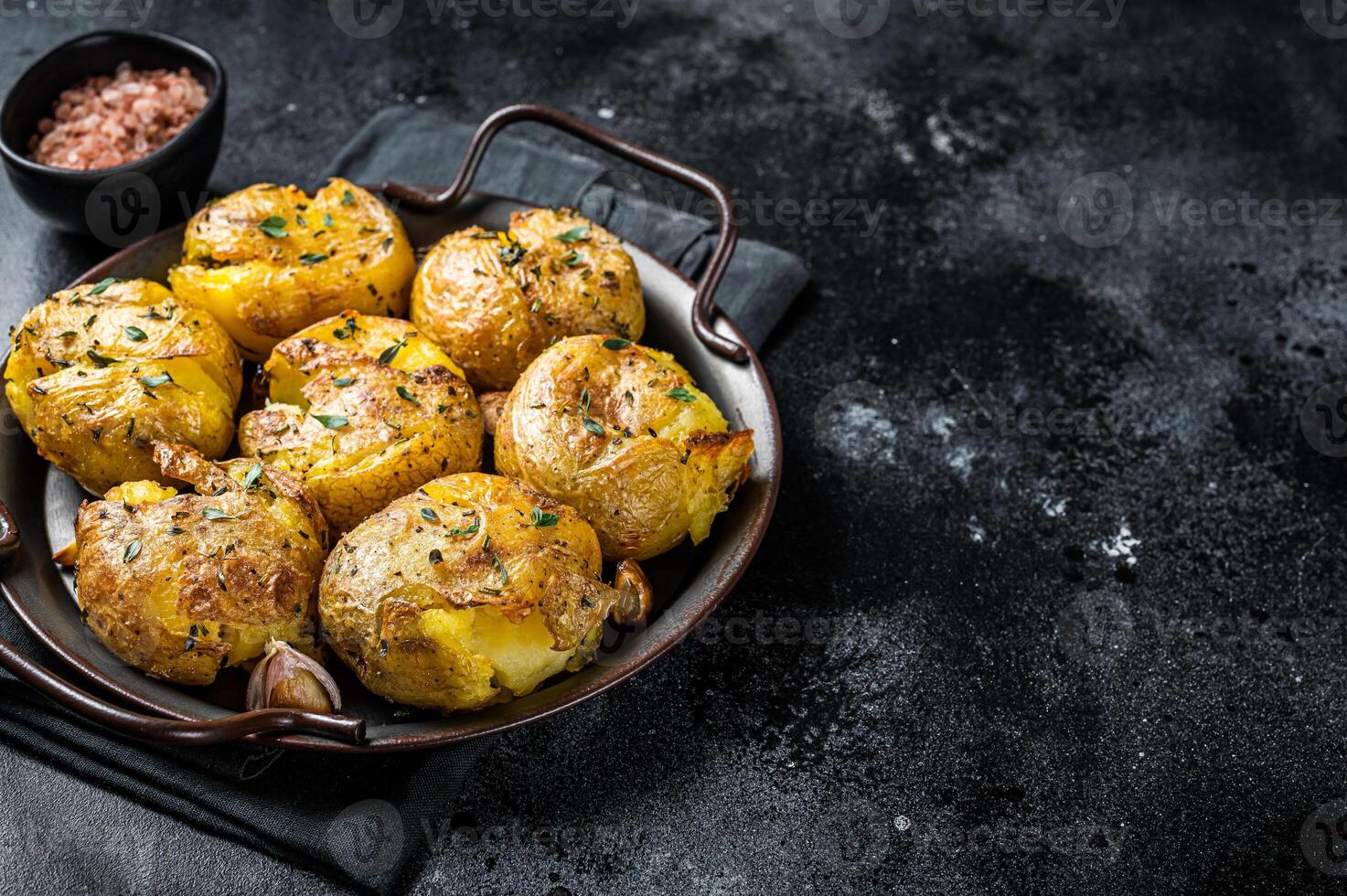 Broken potatoes baked in oil with herbs. Black background. Top view. Copy space photo