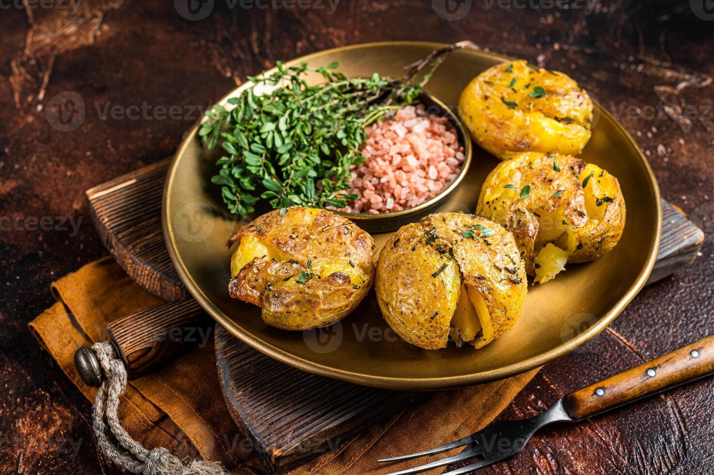 Crushed, smashed potatoes baked with rosemary and thyme on plate. Dark background. Top view photo