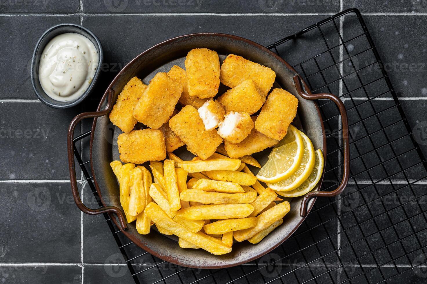 Fish and Chips, Fish Sticks with french fries in a steel tray with sauce. Black background. Top view photo