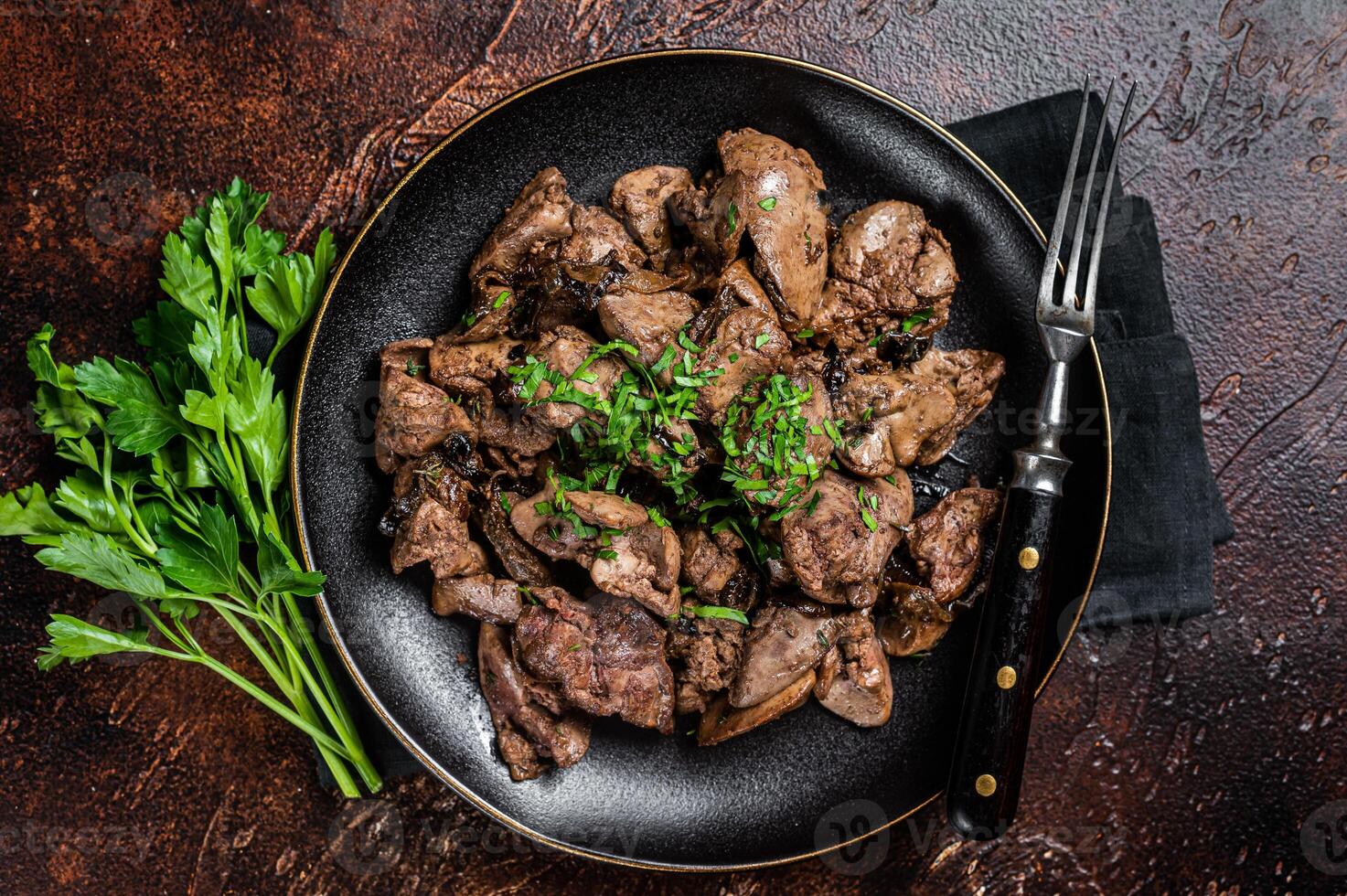 Fried chicken liver with onions and parsley in a plate. Dark background. Top view photo