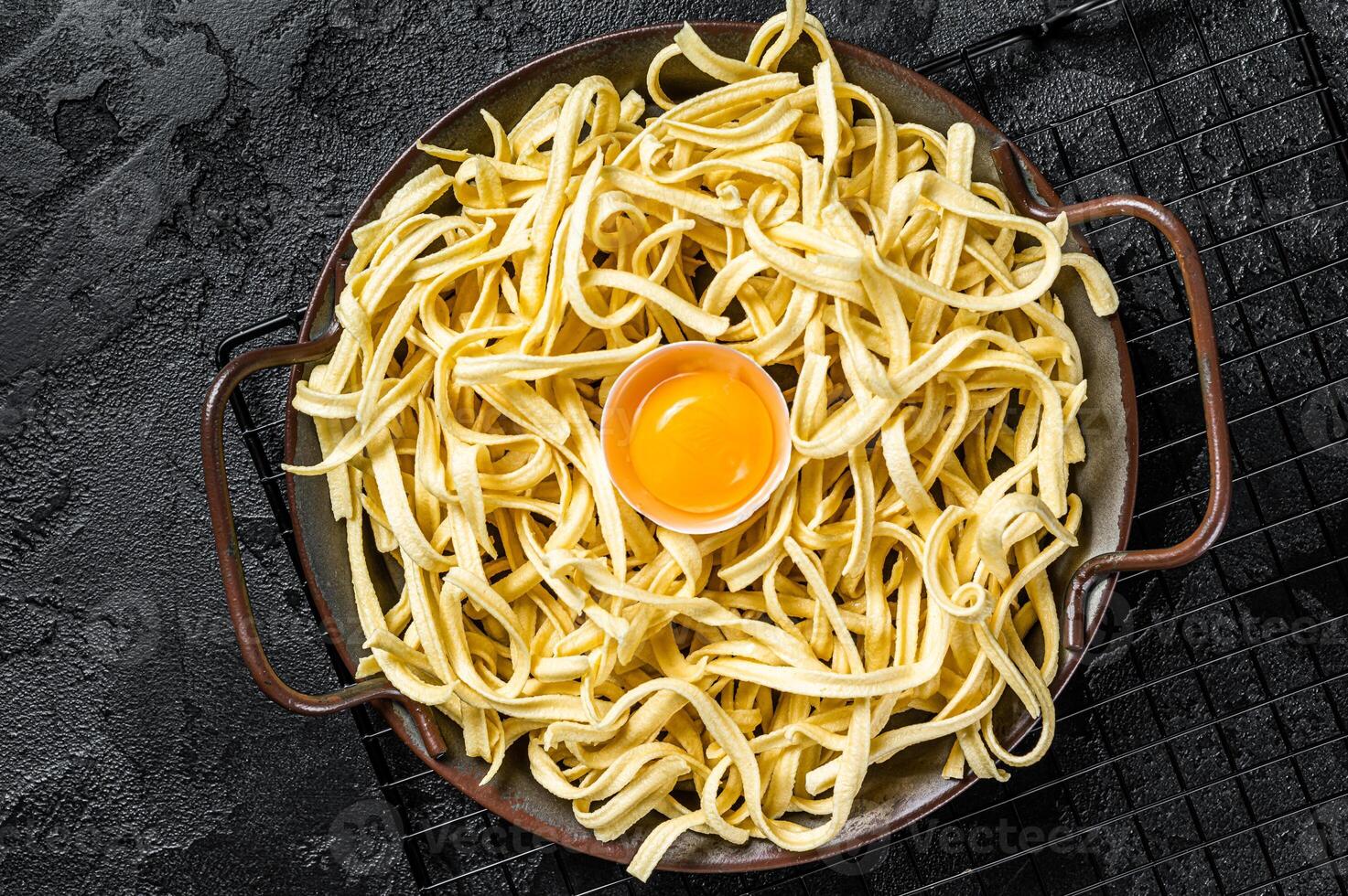 Dry spaetzle egg noodle in a steel tray. Black background. Top view photo