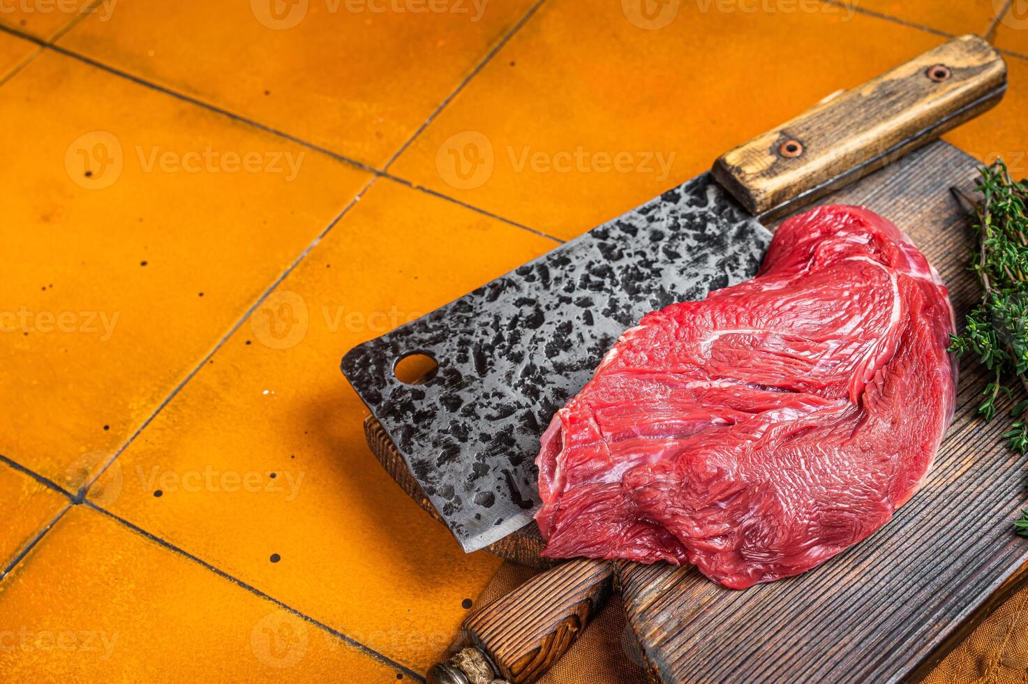 Piece of Raw beef meat for stew with herbs on butcher cutting board. Orange background. Top view. Copy space photo