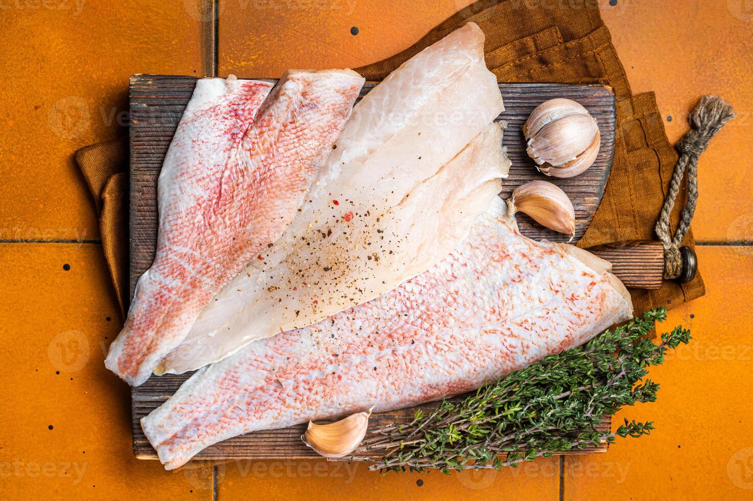 Uncooked ocean red perch fillet, redfish with herbs and spices. Orange background. Top view photo