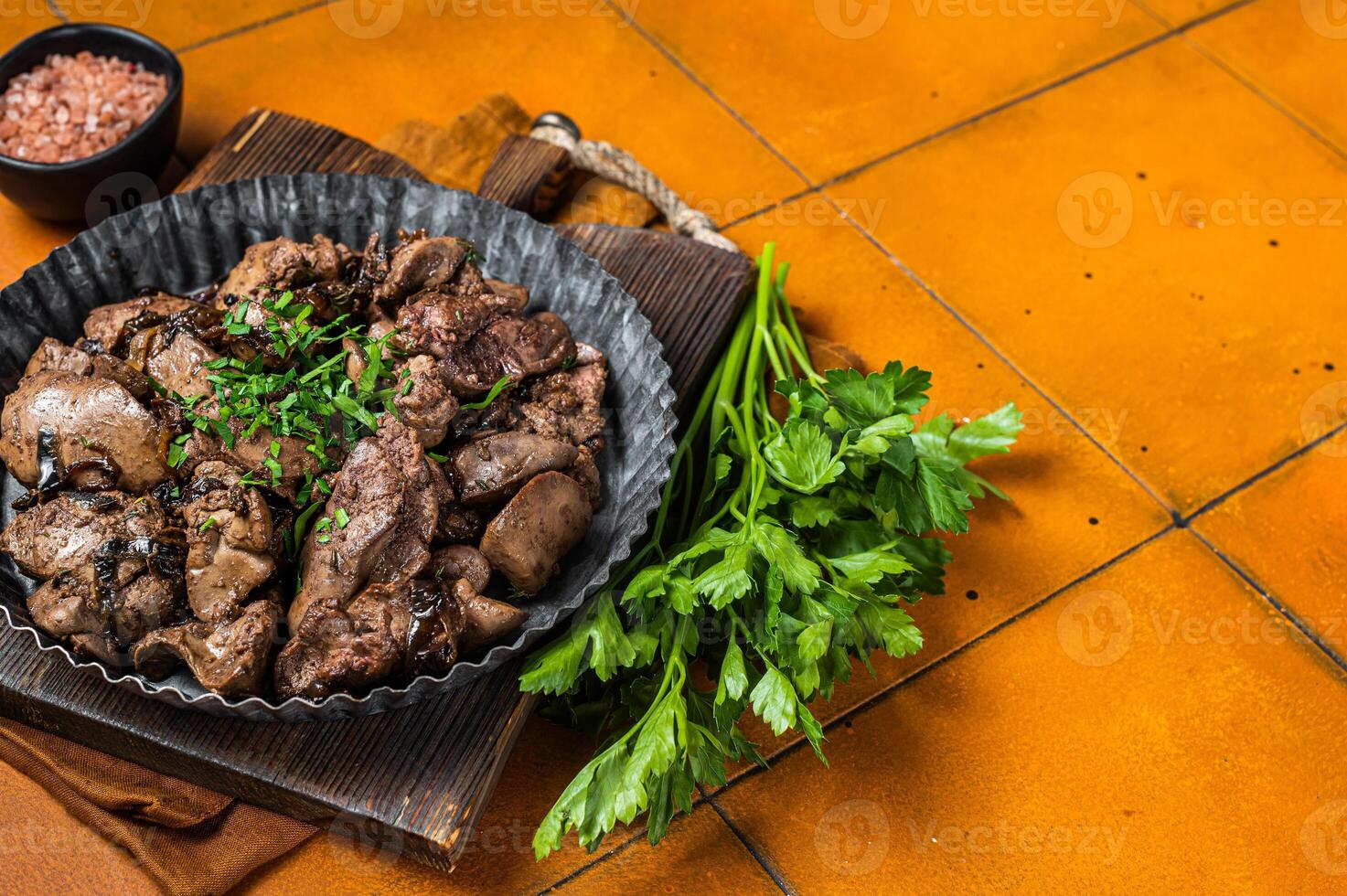 Roast chicken liver with onions and herb in a steel plate. Orange background. Top view. Copy space photo