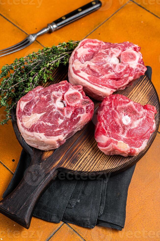 Raw lamb neck chops, fresh mutton meat on a butcher board with herbs. Orange background. Top view photo