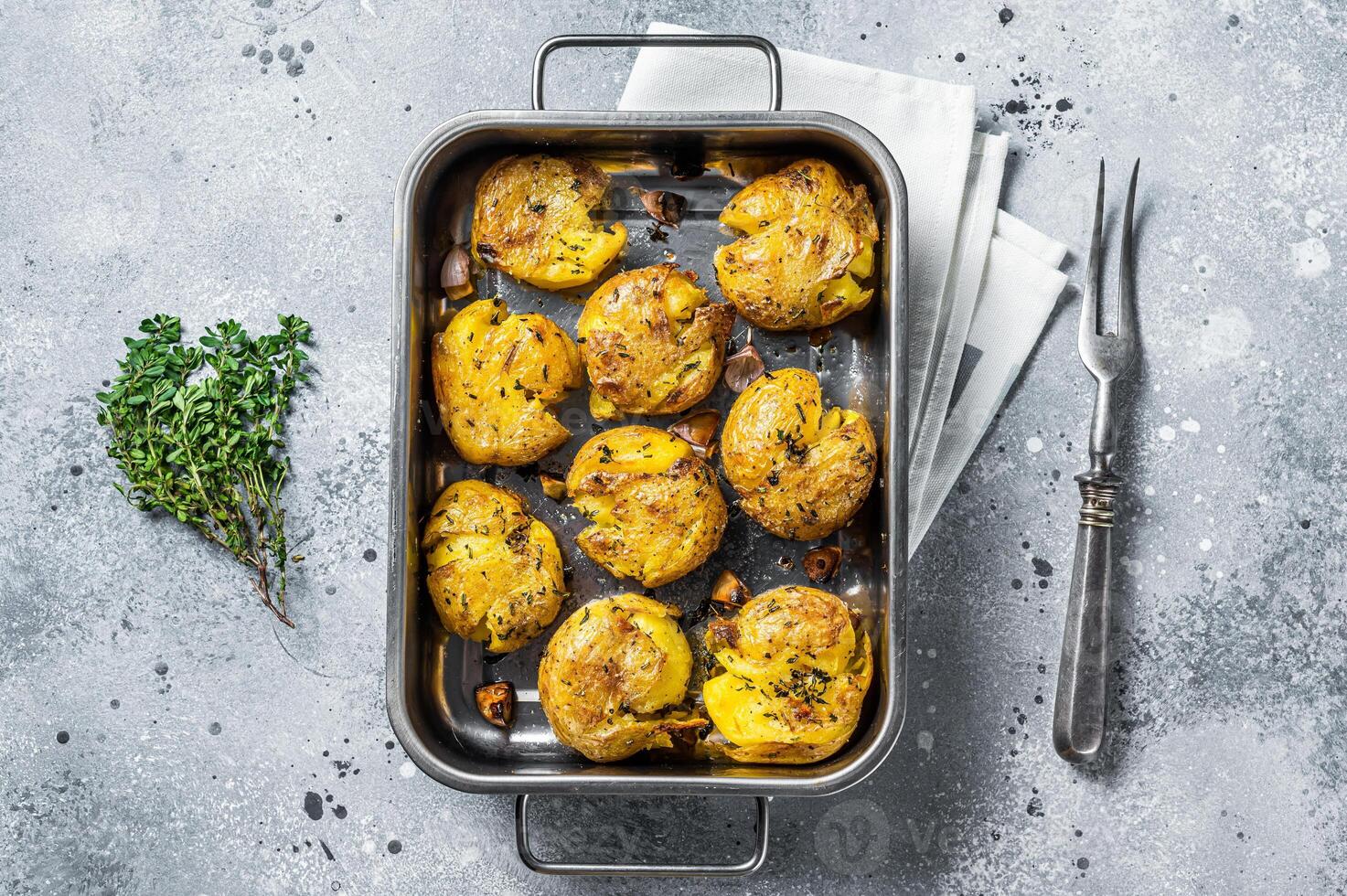 Broken potatoes baked with rosemary and thyme. Gray background. Top view photo