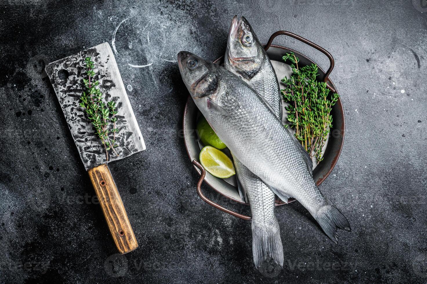Fresh Raw Sea Bass, Labrax fish with herbs and lime. Black background. Top view photo