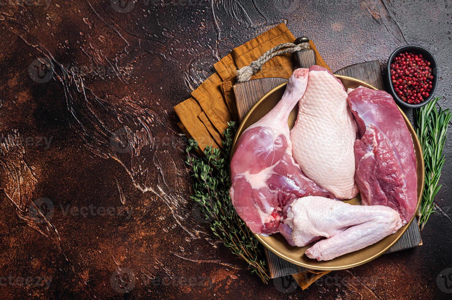 Fresh duck meat parts, raw breast steak, legs, wings in a plate with herbs. Dark background. Top view. Copy space photo