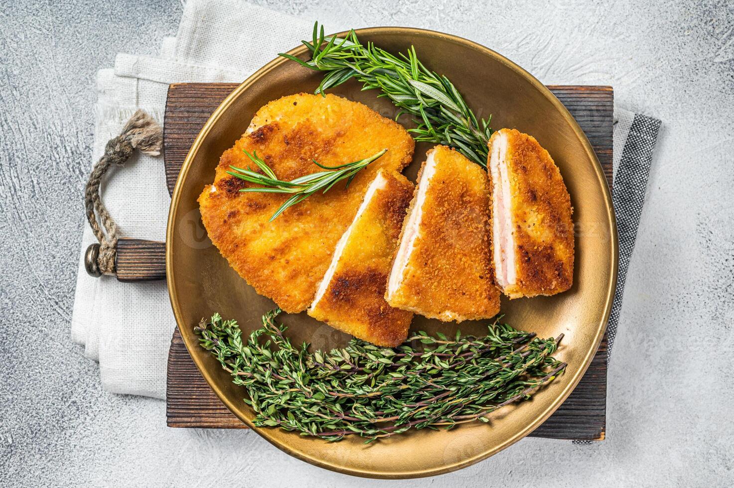 Chicken fried Cordon bleu cutlet with ham and cheese on a plate with herbs. White background. Top view photo