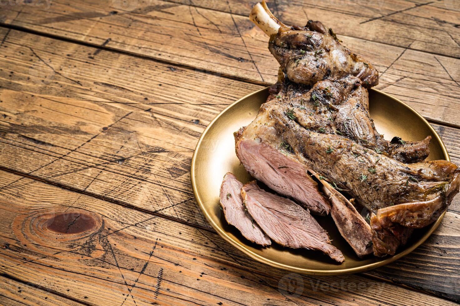 Baked whole lamb shoulder leg with herbs and spices in a steel plate. Wooden background. Top view. Copy space photo