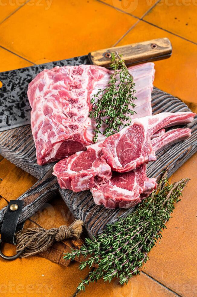 Raw lamb meat chops cutlets on butcher cutting board. Orange background. Top view photo
