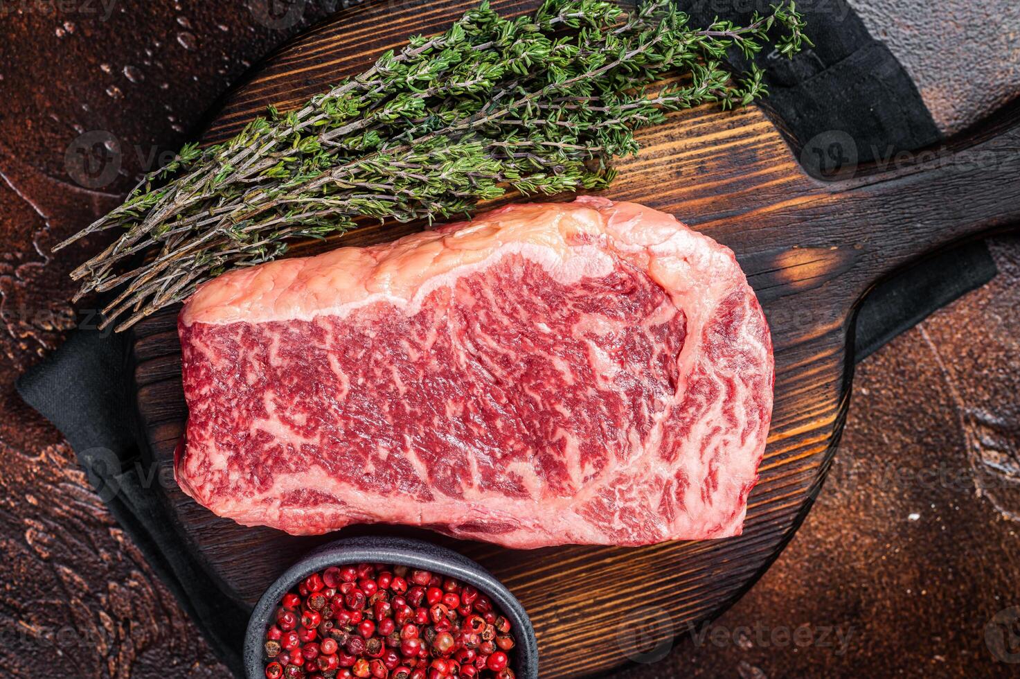 Uncooked Raw striploin or club steak on wooden board with thyme. Dark background. Top view photo