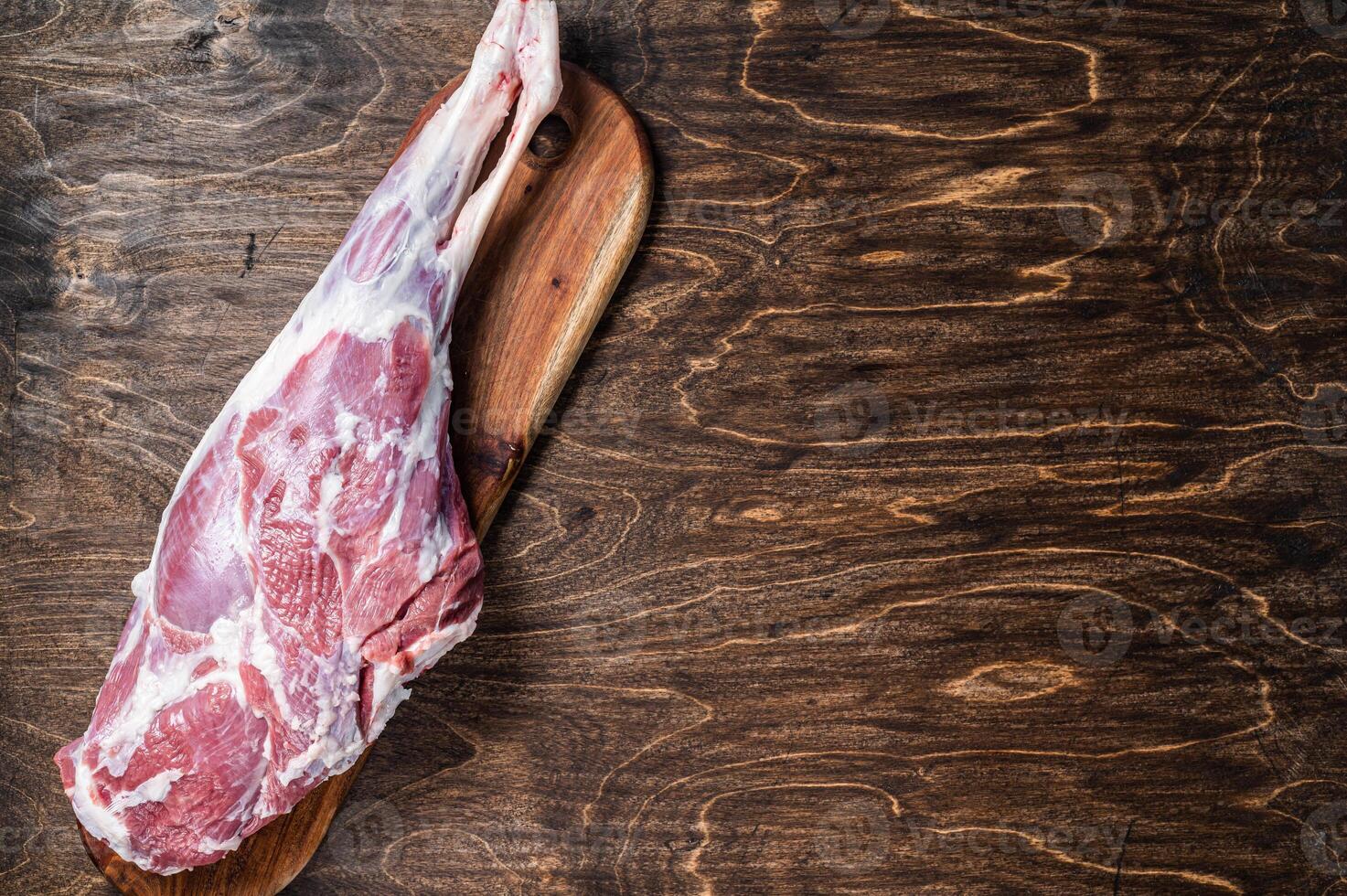 Mutton meat. Raw whole lamb leg thigh on butcher board. Wooden background. Top view. Copy space photo