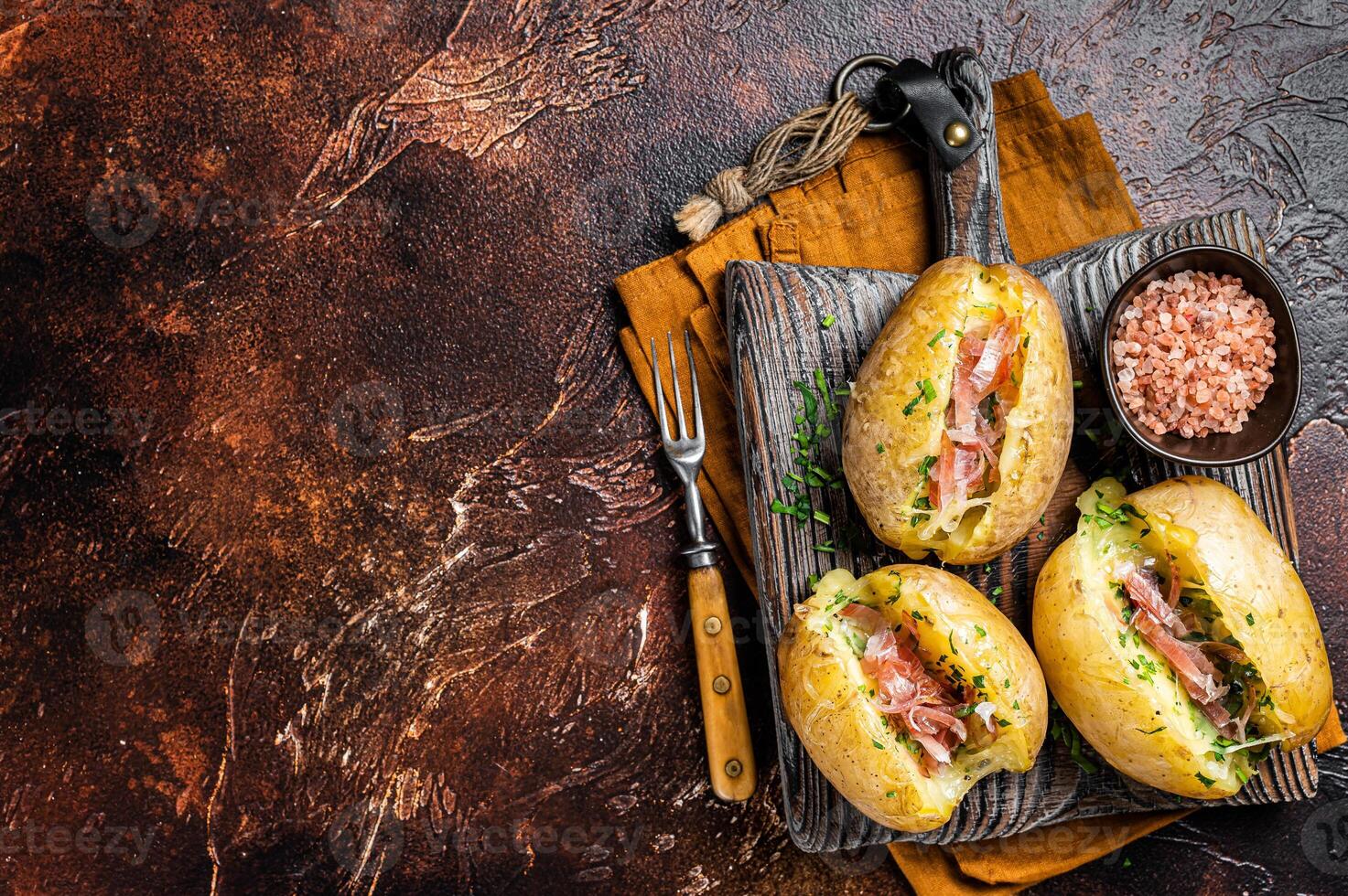 Jacket potatoes baked with cheese, herbs and butter. Dark background. Top view. Copy space photo
