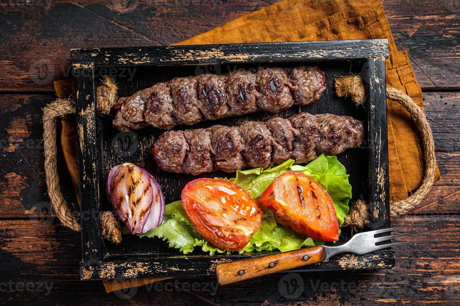 Traditional middle east kefta or kofta kebab, ground beef and lamb meat grilled on skewers served with tomato, salad and onion. Wooden background. Top view photo