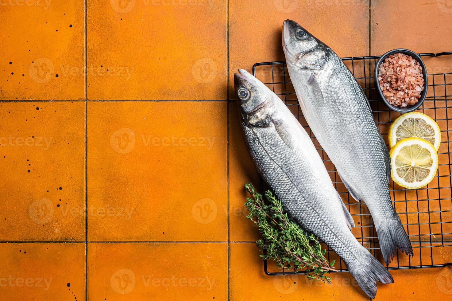 Raw Sea Bass fish with lime and herbs. Orange background. Top view. Copy space photo