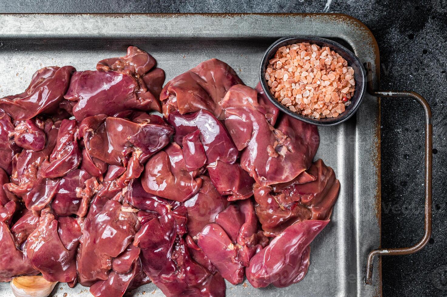 Raw chicken liver meat in steel tray with spices. Black background. Top view photo