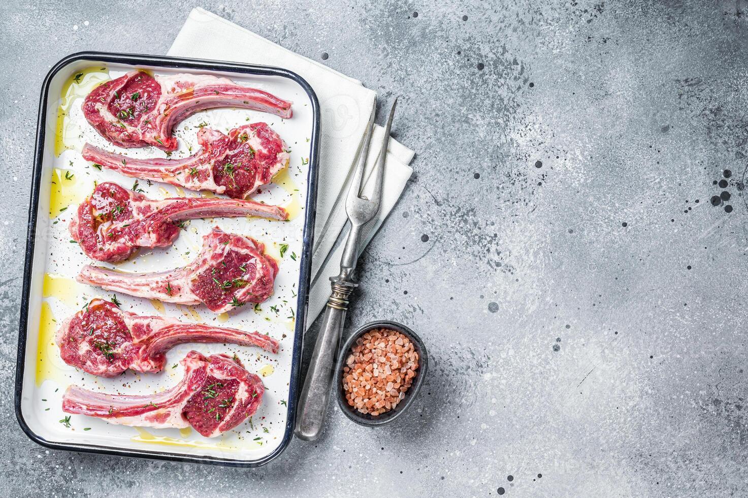 Ready for cooking raw lamb chop steaks with spices and herbs. Gray background. Top view. Copy space photo