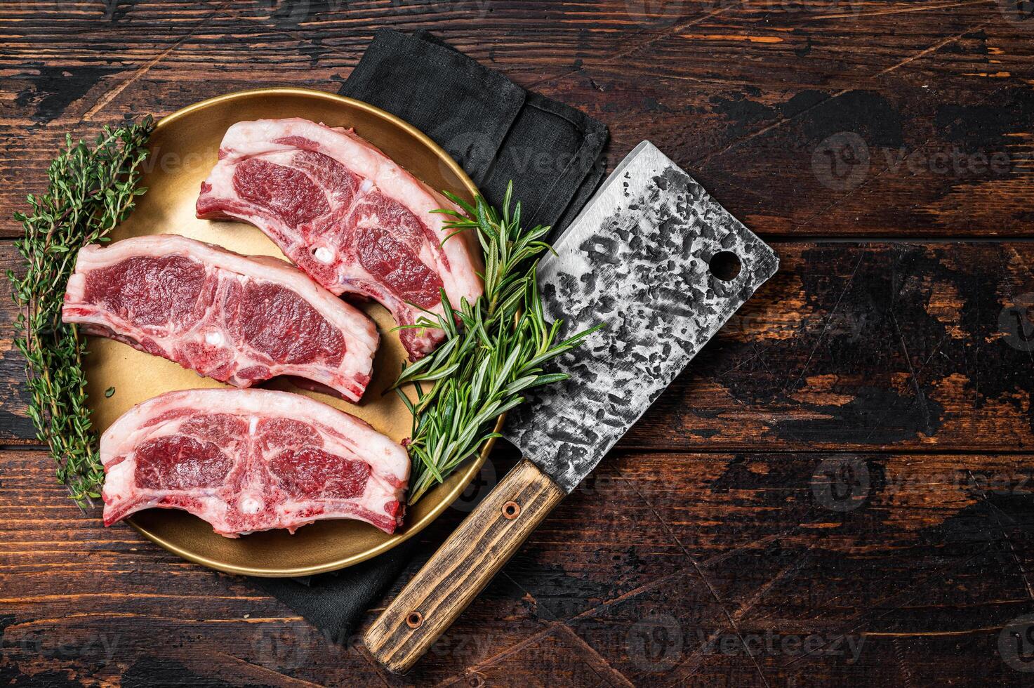 Uncooked Raw lamb loin chops steaks, saddle in plate with rosemary and thyme. Wooden background. Top view. Copy space photo
