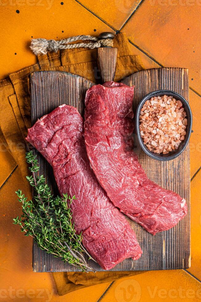 Butcher table with Raw lamb tenderloin Fillet, Mutton loin Meat with thyme. Orange background. Top view photo