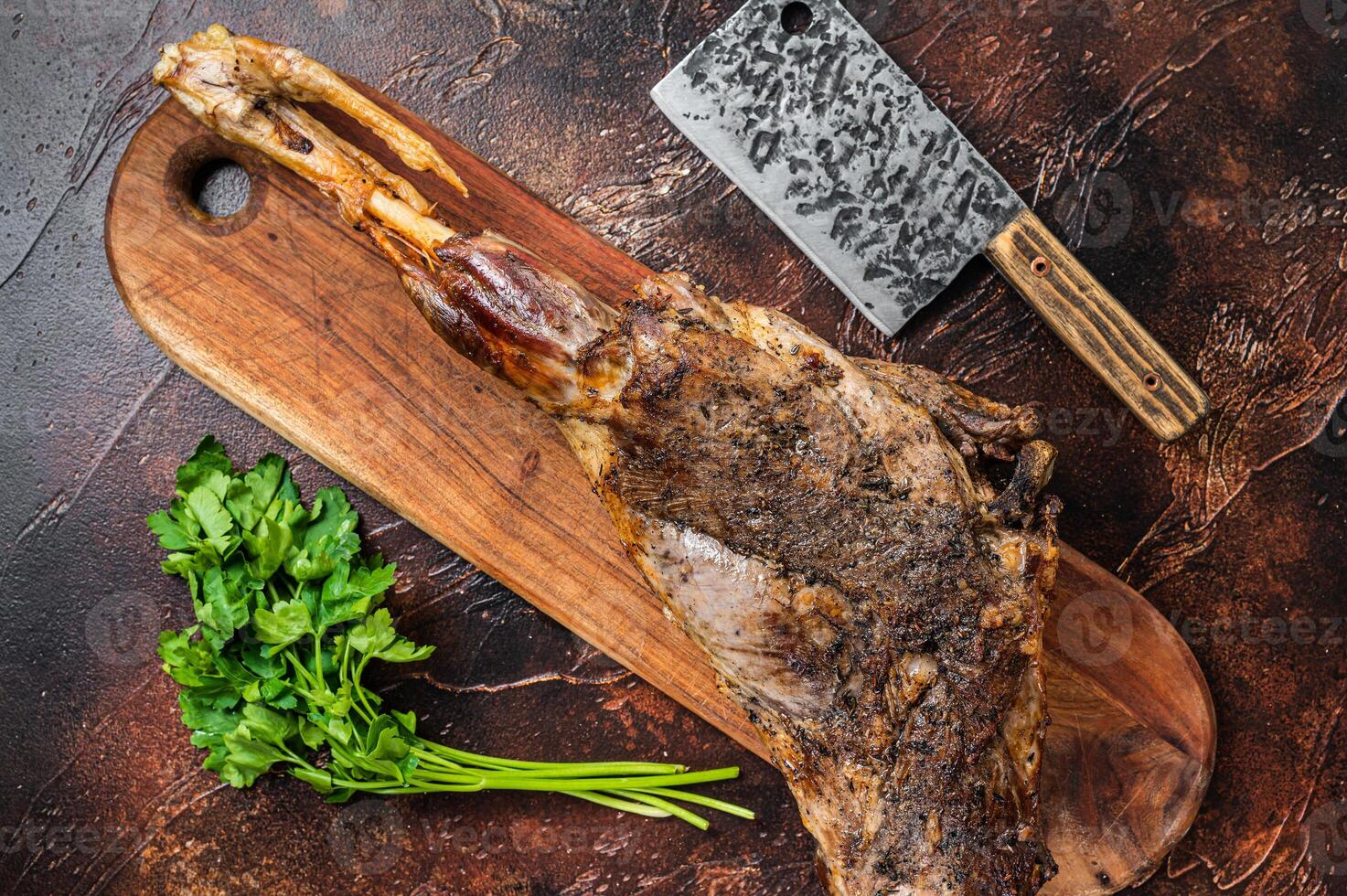 Roast lamb leg meat with herbs and spices on a cutting board. Dark background. Top view photo