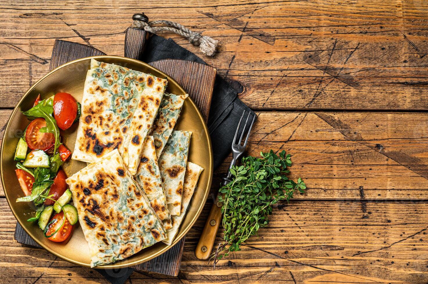 Gozleme flatbread with greens and vegetable salad on garnish. Wooden background. Top view. Copy space photo