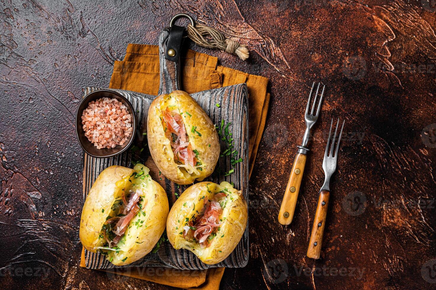 Jacket potatoes baked with cheese, herbs and butter. Dark background. Top view photo