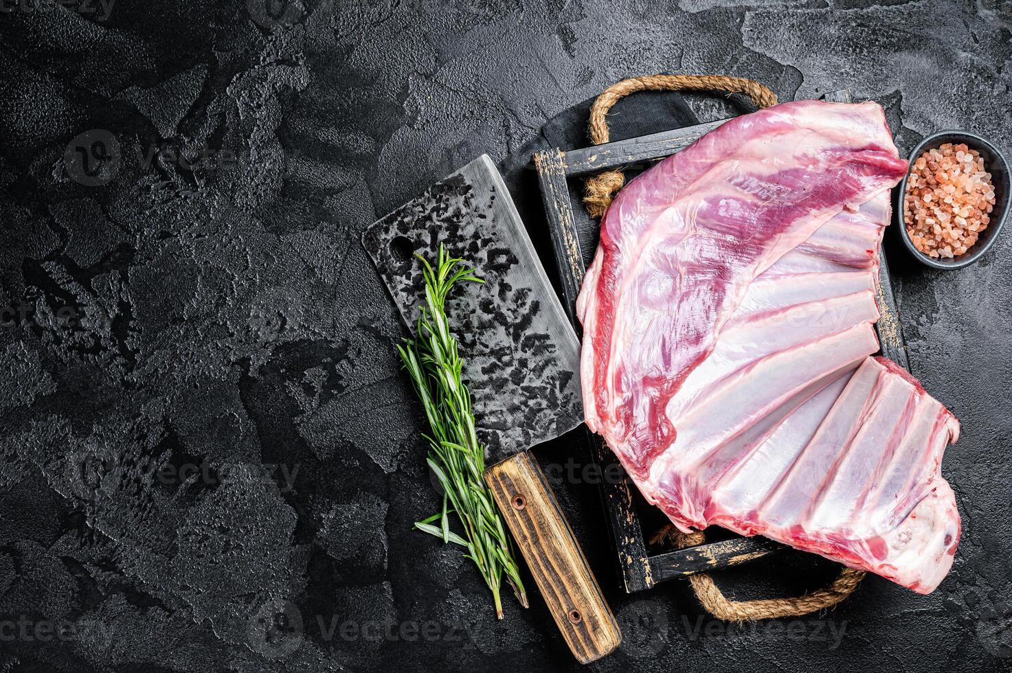 Butcher table with Rack of lamb, raw mutton ribs with meat cleaver. Black background. Top view. Copy space photo