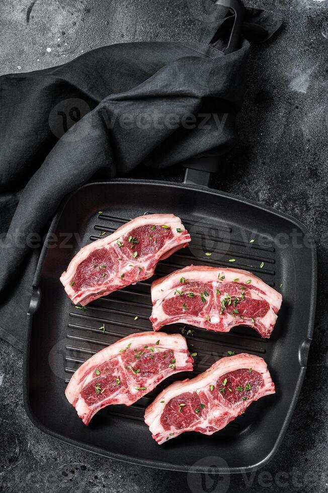 Raw lamb loin rib chops steaks in grill skillet with rosemary and thyme. Black background. Top view photo