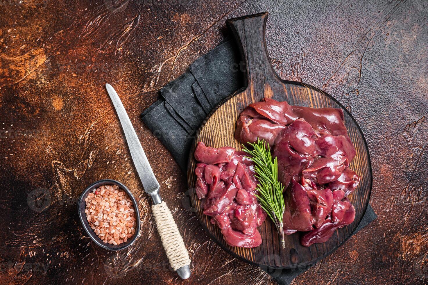 Sliced Raw chicken liver, fresh fowl offals on wooden board. Dark background. Top view photo