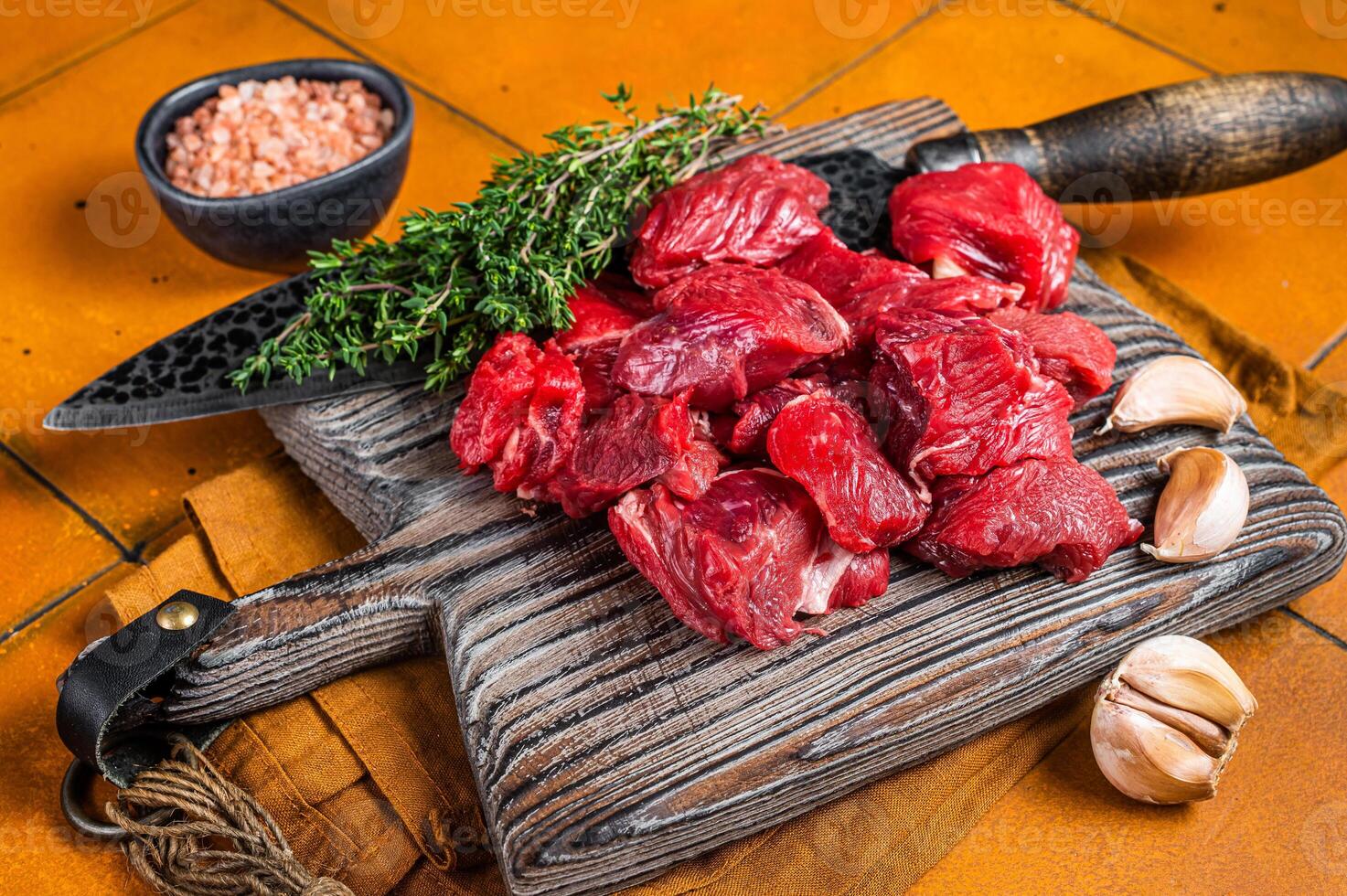 Raw beef meat chopped in cubes on wooden cutting board for cooking stew. Orange background. Top view photo