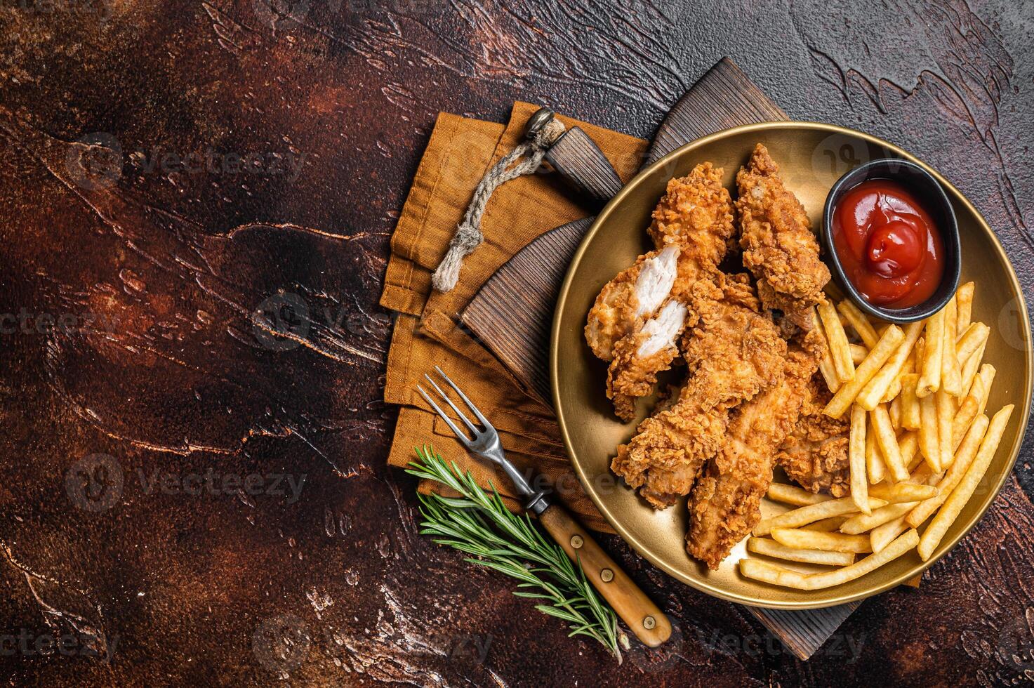 Fried Breaded chicken tender strips with french fries and tomato ketchup on a plate. Dark backgrund. Top view. Copy space photo