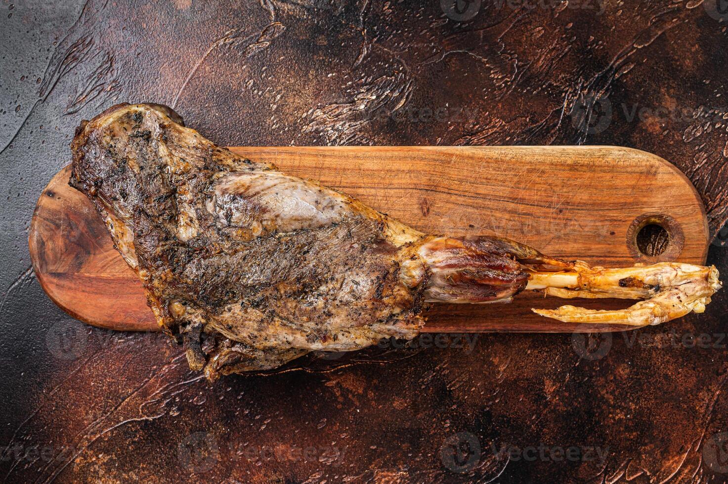 Roast lamb leg meat with herbs and spices on a cutting board. Dark background. Top view photo