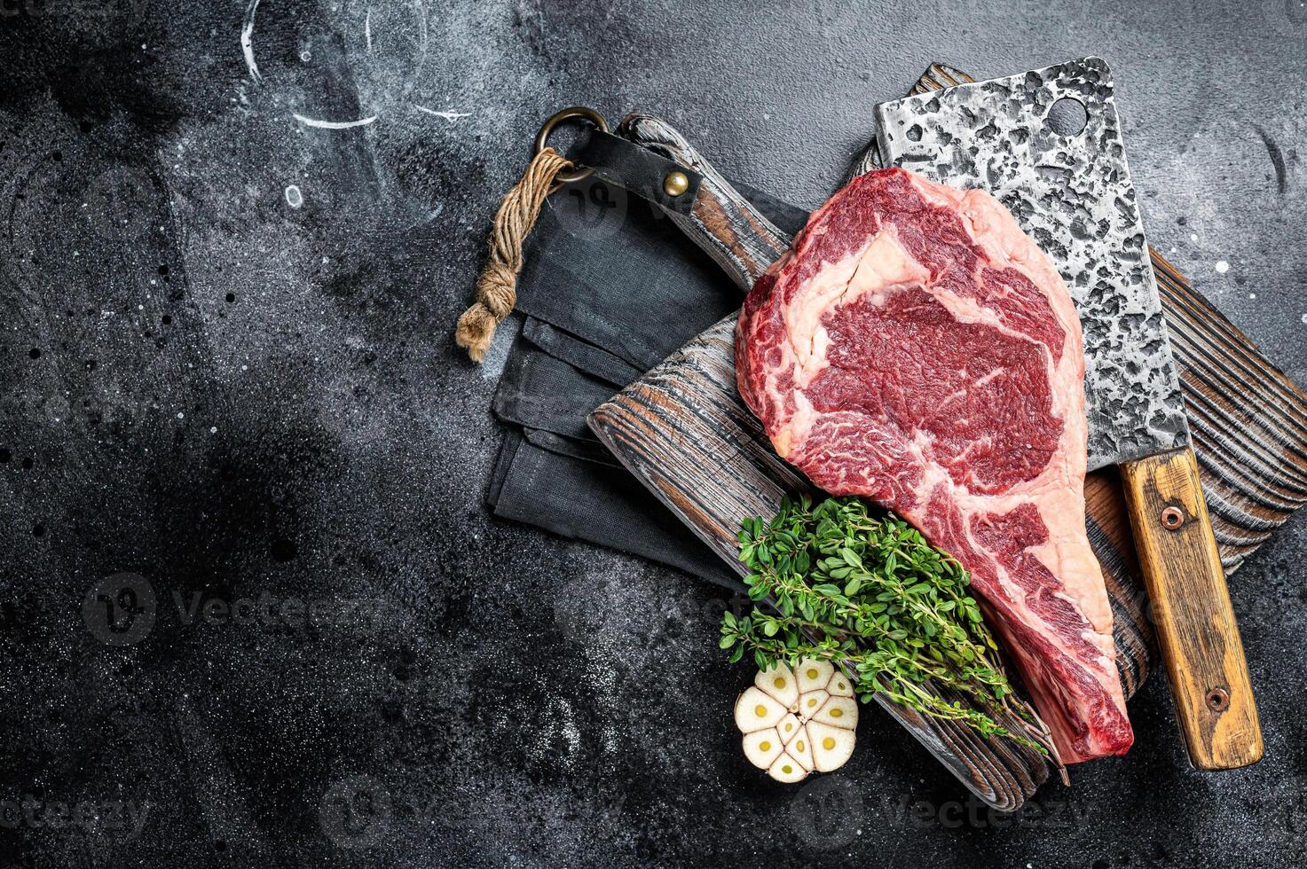 Dry aged Tomahawk rib eye steak, raw beef meat on butcher table. Black background. Top view. Copy space photo