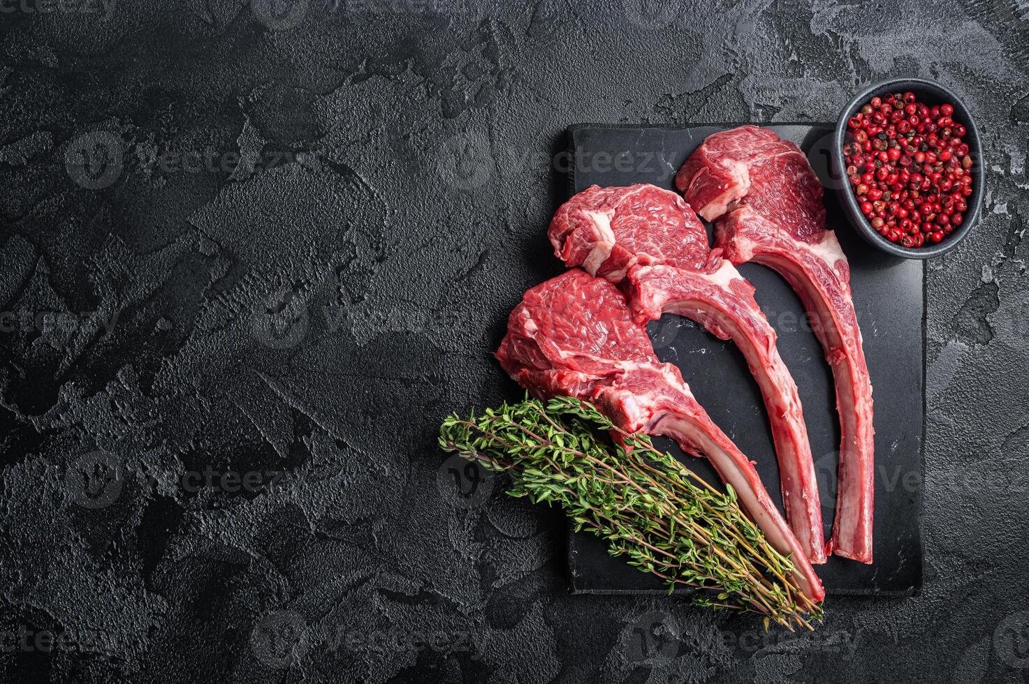 Uncooked Raw Lamb chop steak, mutton cutlet on marble board. Black background. Top view. Copy space photo