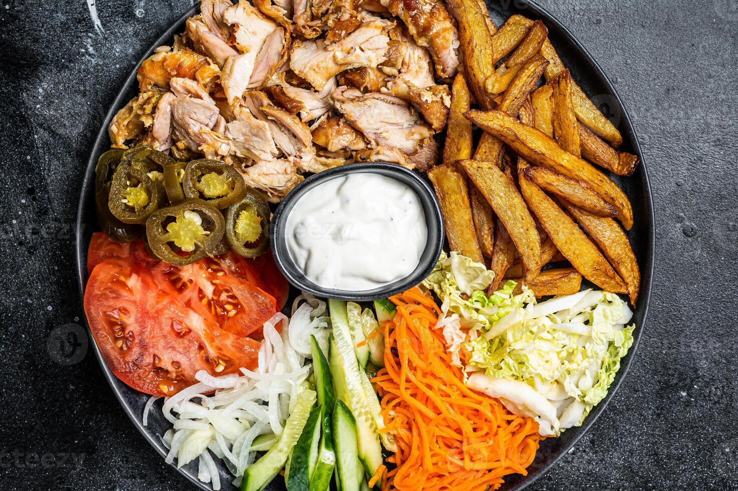 Shawarma Doner kebab on a plate with french fries and salad. Black background. Top view photo