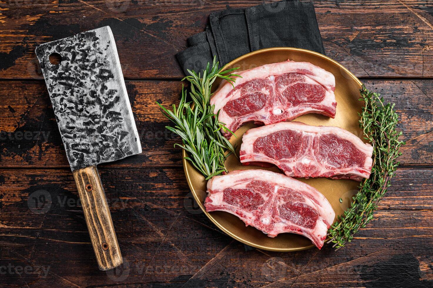 Uncooked Raw lamb loin chops steaks, saddle in plate with rosemary and thyme. Wooden background. Top view photo