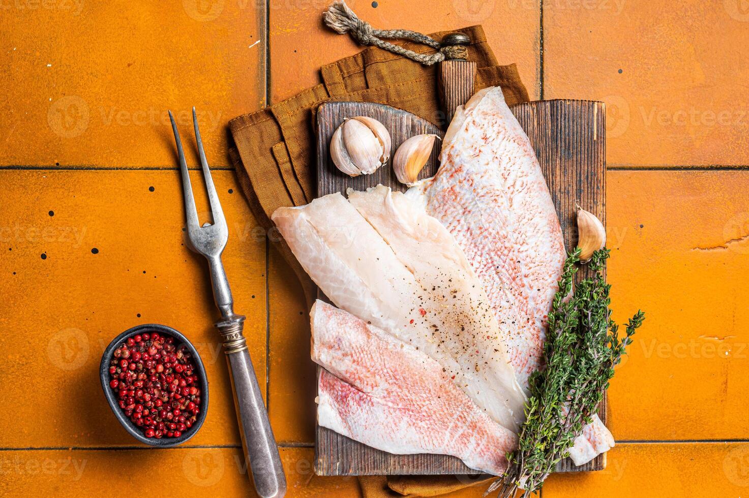 Uncooked ocean red perch fillet, redfish with herbs and spices. Orange background. Top view photo