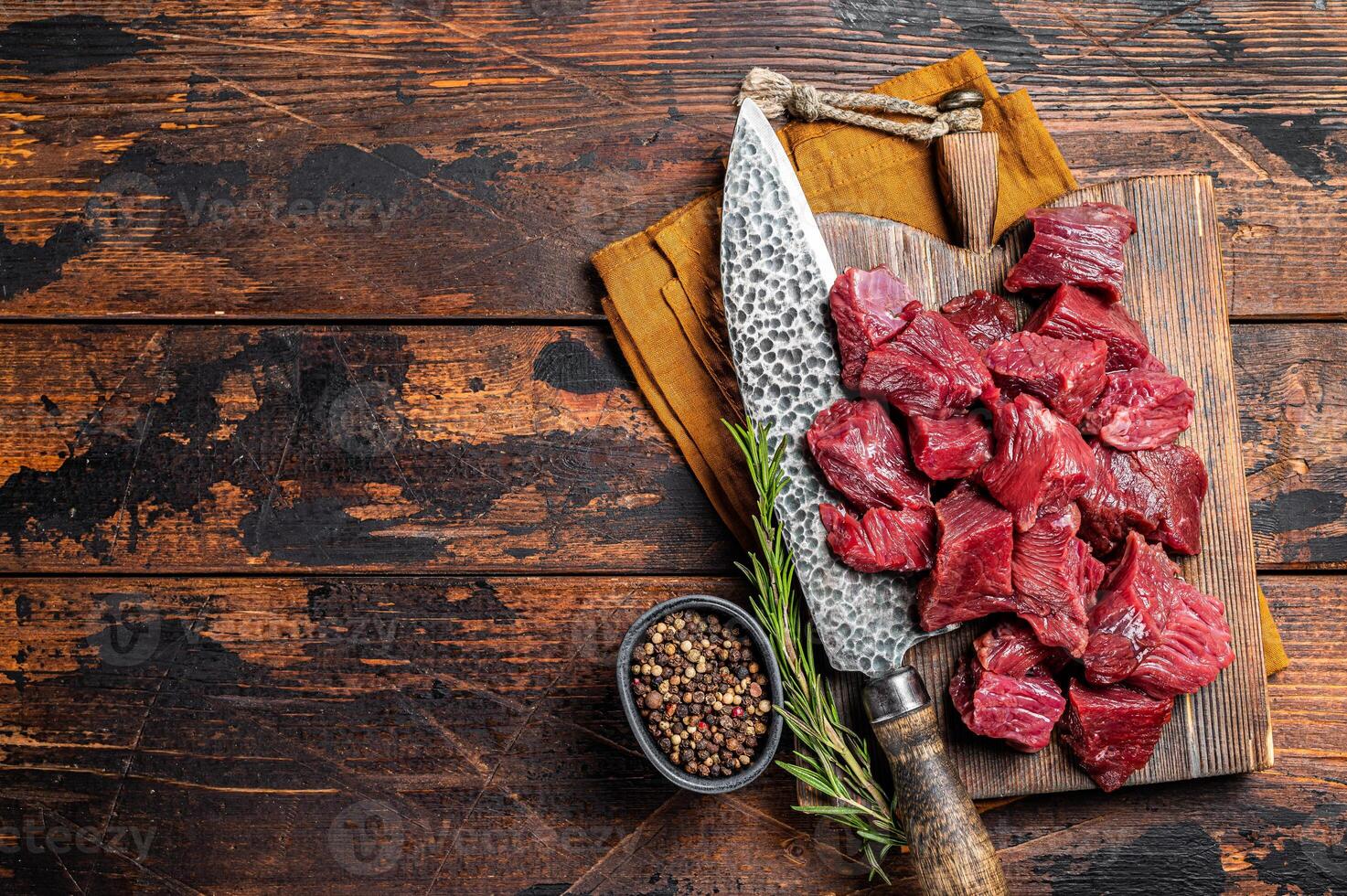 Sliced Raw venison dear meat for a stew, game meat on butcher cutting board. Wooden background. Top view. Copy space photo