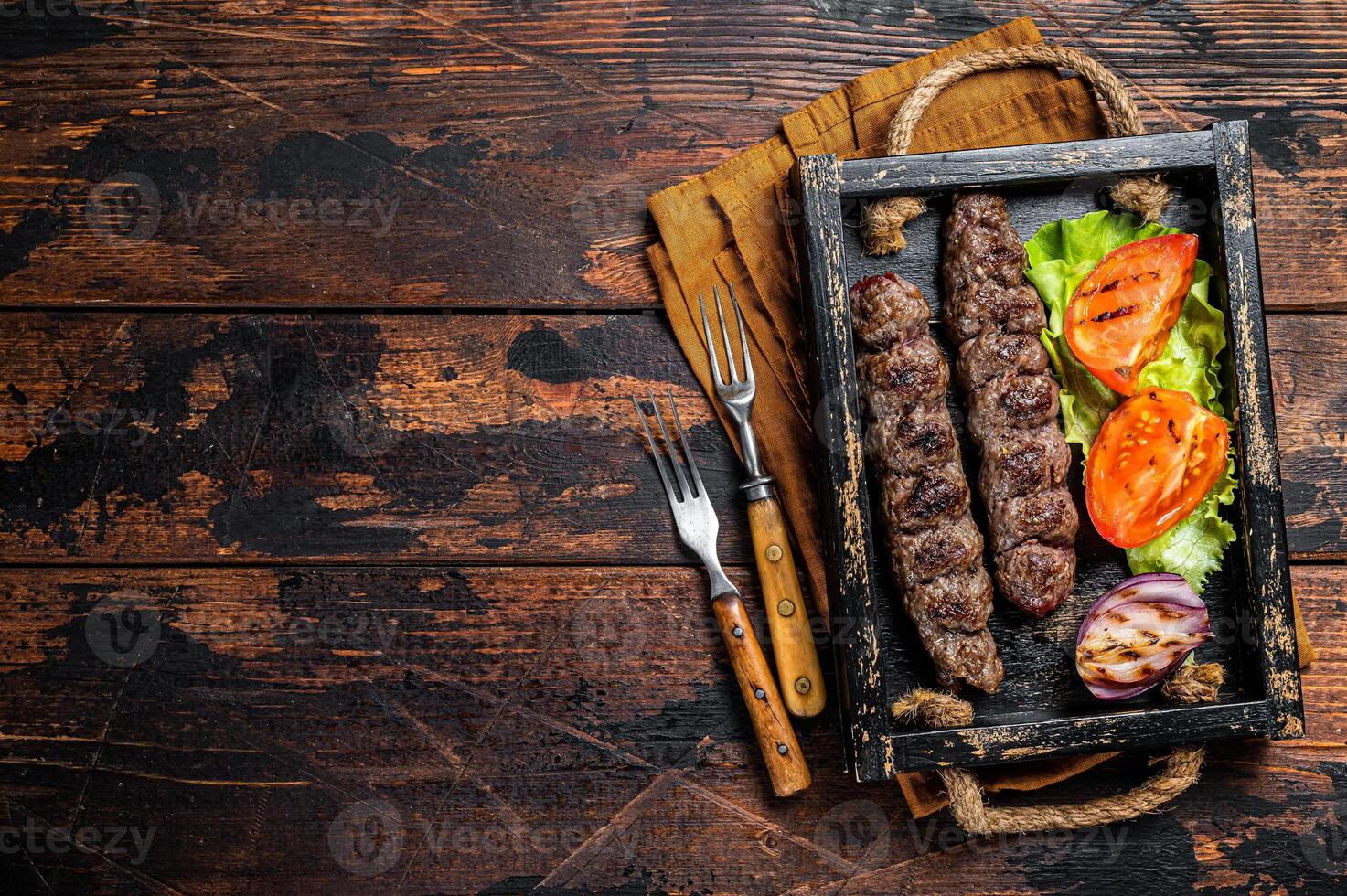 Traditional middle east kefta or kofta kebab, ground beef and lamb meat grilled on skewers served with tomato, salad and onion. Wooden background. Top view. Copy space photo