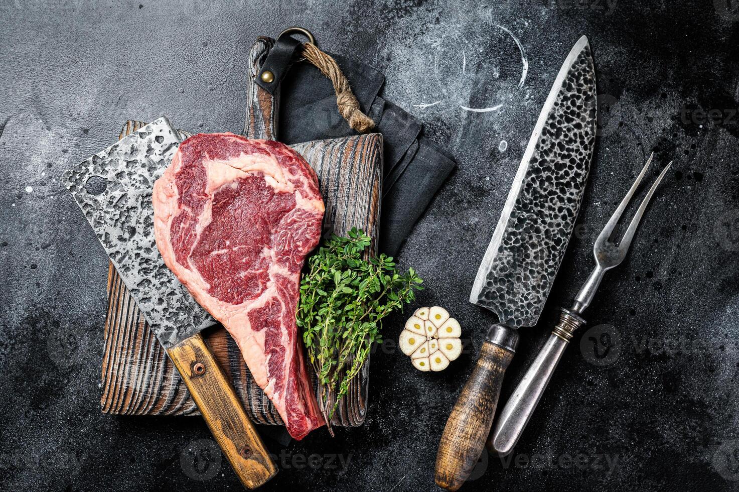 Dry aged Tomahawk rib eye steak, raw beef meat on butcher table. Black background. Top view photo