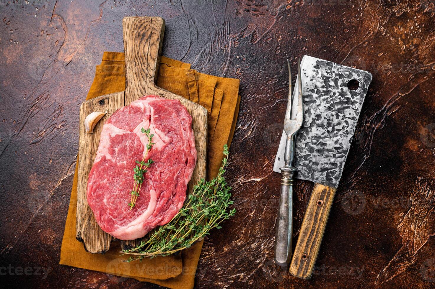 Fresh Marbled Rib eye steak with herbs on butcher cutting board, raw beef meat. brown background. top view photo