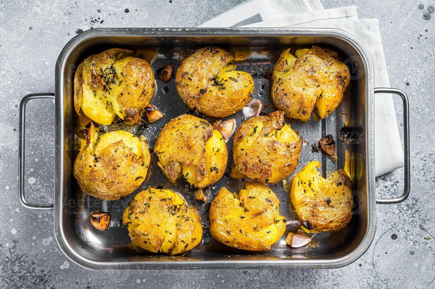 Broken potatoes baked with rosemary and thyme. Gray background. Top view photo