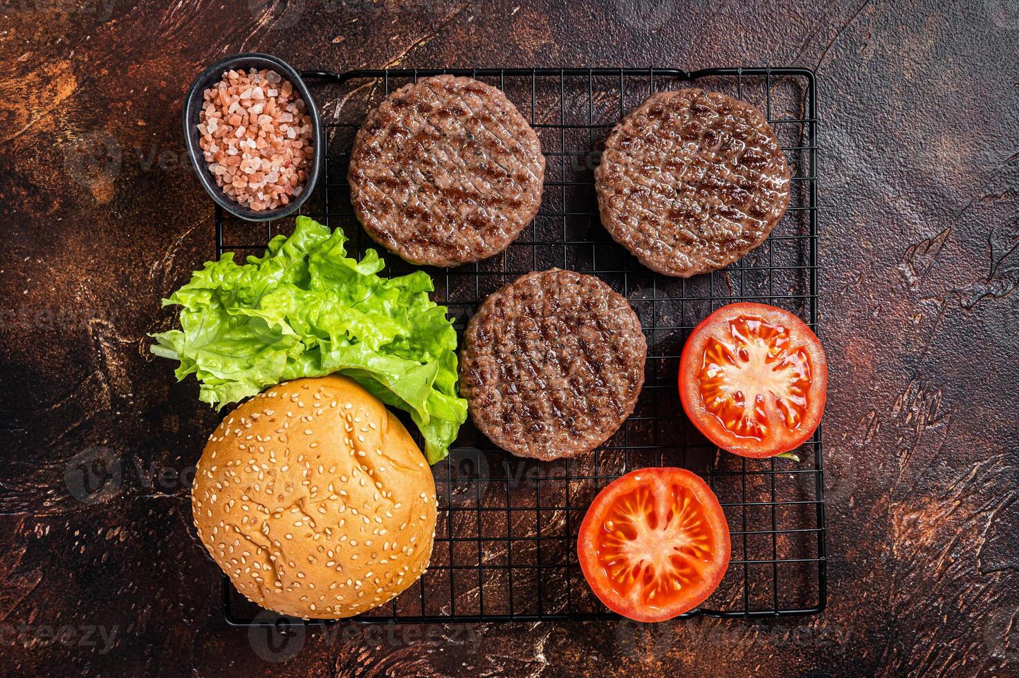 Grilled hamburger patties with tomatoes and seasonings on kitchen table. Dark background. Top view photo