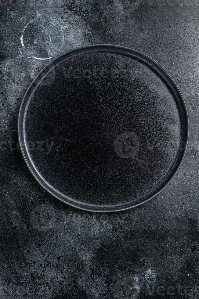Empty black craft plate on table. Table setting. Black background. Top view. Copy space photo