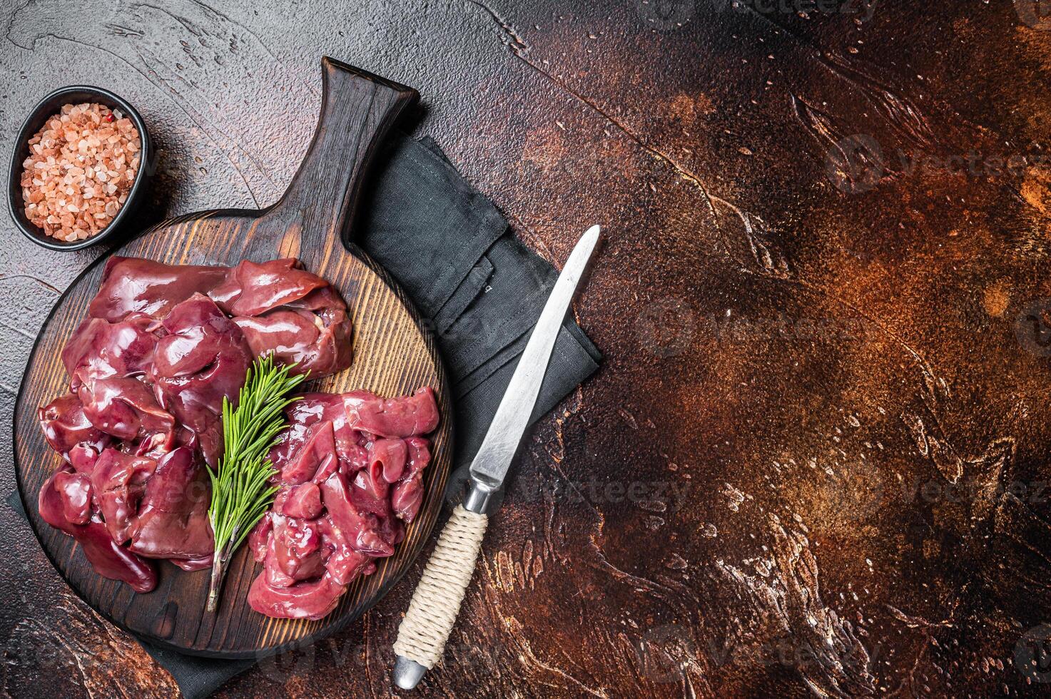 Sliced Raw chicken liver, fresh fowl offals on wooden board. Dark background. Top view. Copy space photo