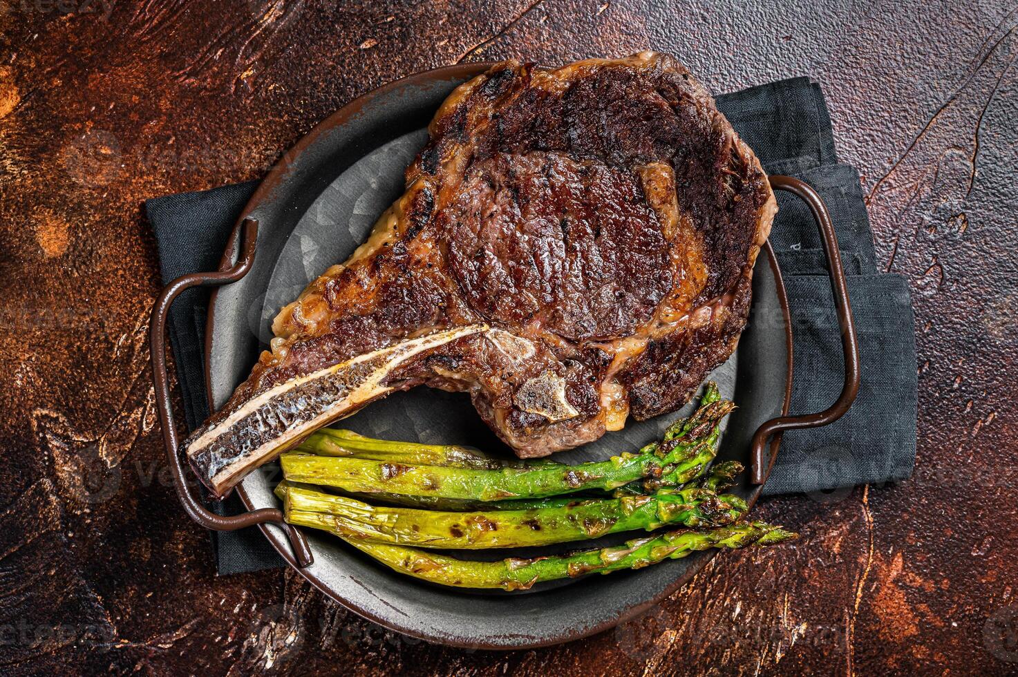 BBQ Grilled Tomahawk or Cowboy with bone beef steak, roasted asparagus. Wooden background. Top view photo